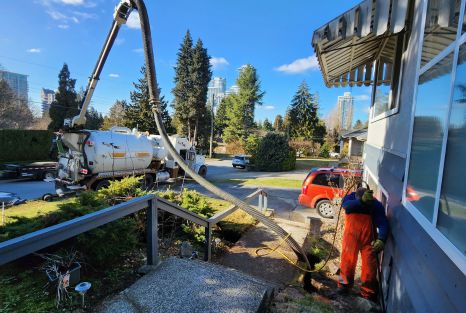 Vacuum-service equipment positioned beside a house with a long hose run across the property.