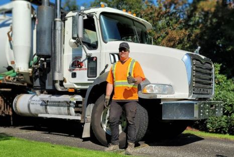 Vac truck operator in high-visibility gear beside a service truck.